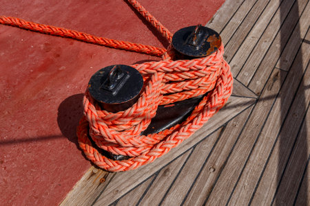 A fragment of the ship and mooring bollard on a wooden deck with red rope. Mooring of ships and...