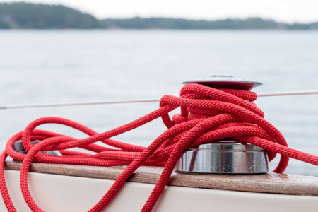 Sailboat winch with red rope of genoa headsail sheet on yacht deck. Detail, low depth of focus.