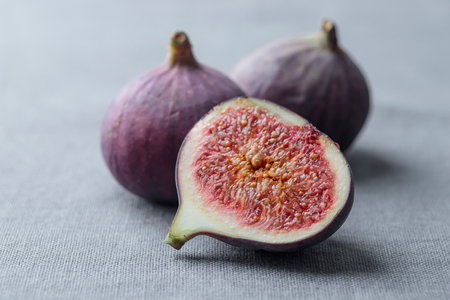 Ripe fresh organic fig fruits with a sliced piece on a gray background with a soft light, simple minimalistic shot with a copy spaceの写真素材