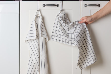 A young woman is drying her hands in the kitchen on a cotton towel hanging on the cabinet door. A minimalistic white kitchen cabinet beneath the sink holds a dish rag or towels, blending style with functionality and keeping essentials within easy reachの写真素材