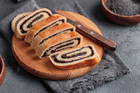 Home baked poppy seed roll, bejgli in slices, traditional Hungarian, Eastern European Christmas and Easter sweet bread on a wooden cut board. Closeup on the table. Horizontal side viewの写真素材