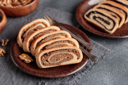 Home baked roll, bejgli in slices, traditional Hungarian sweet bread stuffed with walnut and poppy seed filling. Eastern European Christmas and Easter sweet bread. Closeup on the table. Horizontal side view on a gray backgroundの写真素材