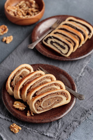 Home baked roll, bejgli in slices, traditional Hungarian sweet bread stuffed with walnut and poppy seed filling. Eastern European Christmas and Easter sweet bread. Closeup on the table. Vertical top view on a gray backgroundの写真素材