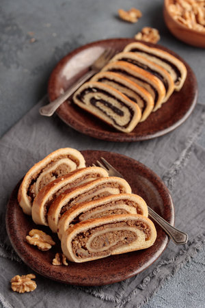 Home baked roll, bejgli in slices, traditional Hungarian sweet bread stuffed with walnut and poppy seed filling. Eastern European Christmas and Easter sweet bread. Closeup on the table. Vertical top view on a gray backgroundの写真素材
