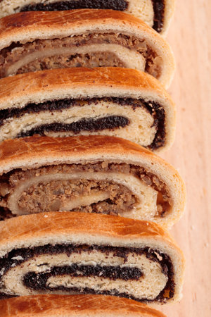 Bejgli, home-baked roll, traditional Hungarian, Eastern European Christmas and Easter sweet bread in slices stuffed with ground walnuts and poppy seed filling on wooden cut board on a gray background. Vertical close up top viewの写真素材