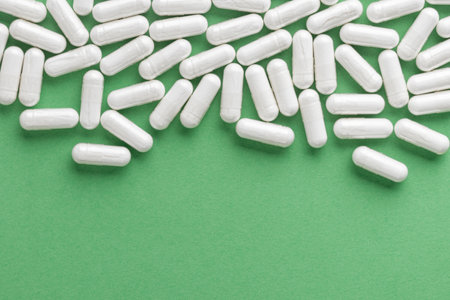 Scattered white medicine, pills or capsules on green table. Mock up background from top view with a...