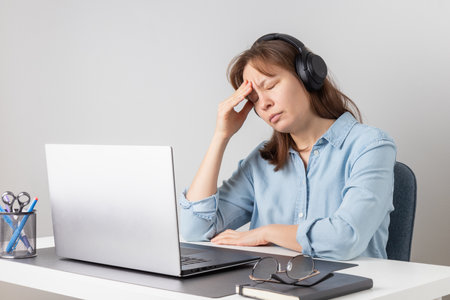 An overworked female freelancer is tired and stressed behind her laptop. Exhaustion and burnout problem of remote working. Woman struggles with fatigue and job-related stressの写真素材