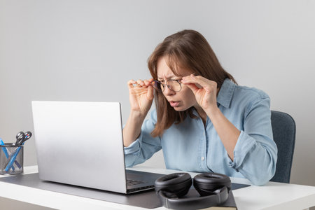 What is wrong. Anxious frustrated female office worker sitting at desk with pc laptop and getting angry. Irritated freelancer woman looking at laptop computer with disappointment and frustrationの写真素材