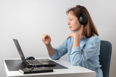 A calm smiling woman with headphones using laptop, looking at PC screen, remote hardworking freelancer works from home. Correct posture, good environmentの写真素材