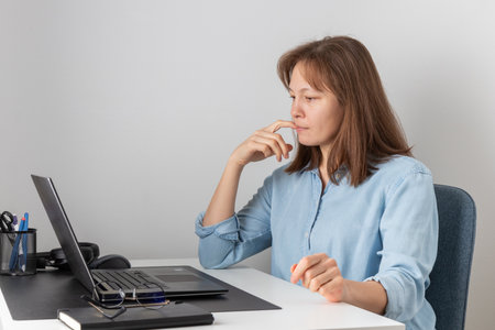 A woman using laptop, looking at PC screen and waiting, thinking, studying online or having virtual call meeting remote working from home, habit of biting nailsの写真素材