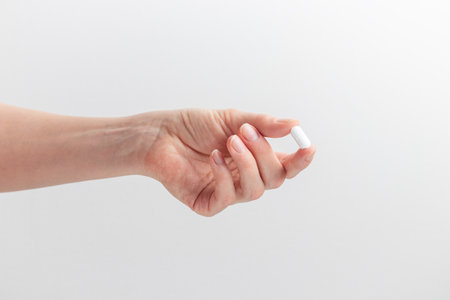 Female hand holding white pill with fingers on white background. Concept of health care, dietary supplements, treatment of depression and diseases. High quality photo bannerの写真素材