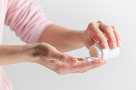 A woman's hand pours white pills from a bottle on a white background. Healthcare concept, nutritional supplements, treatment of depression and diseaseの写真素材