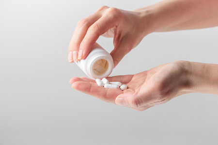 A woman's hand pours white pills from a bottle on a white background. Healthcare concept, nutritional supplements, treatment of depression and diseaseの写真素材