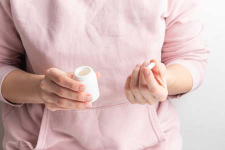 Female hand holding white bottle with pills on white background. Concept of health care, dietary supplements, treatment of depression and diseases. High-quality photo bannerの写真素材