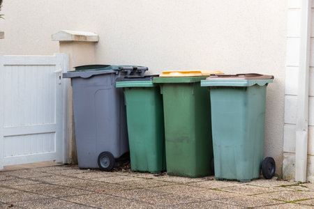 Different colored waste bins are neatly arranged along the side of a residential street. These containers for recycling and waste disposal. Paris, Franceの写真素材