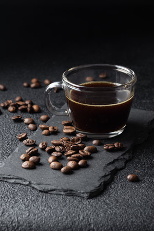 Dark coffee in a glass cup, black espresso and roasted coffee beans on black table, close up. Vertical banner with copy spaceの写真素材