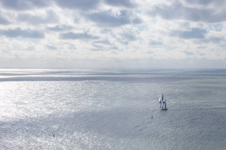 Aerial view of two sailboats floating together in calm sea. Nearby, kite surfers soar with colorful sails, carving waves and leaping into the airの写真素材