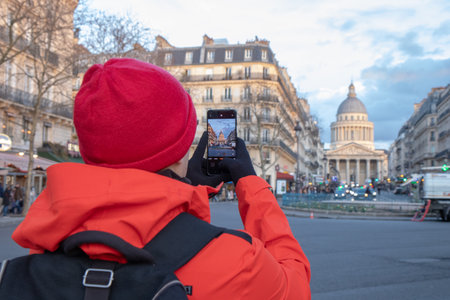 A lonely tourist in red coat takes a photo by his smartphone of the Pantheon in Paris, France, capturing its grand neoclassical architecture and timeless beautyの写真素材