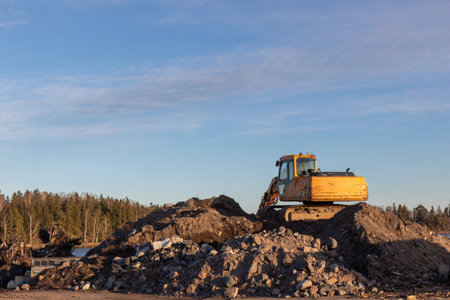 Yellow excavator groundworks on sunset, digger on construction site on blue sky. Heavy construction...