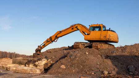 Yellow excavator groundworks on sunset, digger on construction site on blue sky. Heavy construction equipment on excavation on construction site, open-pit miningの写真素材