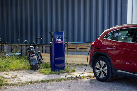 Red electric car parked at a charging station, plugged in and charging electricity, showcasing clean energy and sustainable urban transportationの写真素材