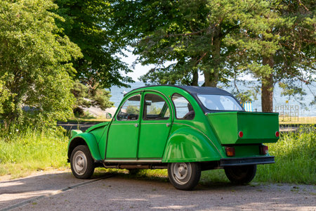 Vintage green retro car parked on a street with lush green foliage in the background, creating a...