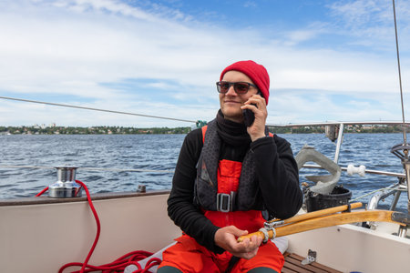 Young man in red hat steering a sailboat with wooden tiller on the open waters of the Gulf of...