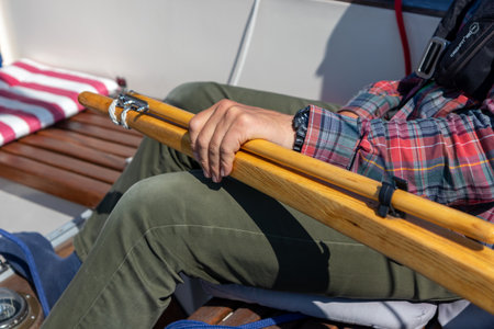 Skilled young man steering a sailboat with wooden tiller on the open waters of the Gulf of Finland. Good sailing experience, maritime adventure, summer leisure, connection to the seaの写真素材