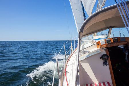 Luxury sailing yacht under genoa and mainsail cutting through waves of the Baltic Sea, Gulf of Finland. View from deck to bow, mast, and sails, emphasizing speed, motion, and yachting adventureの写真素材