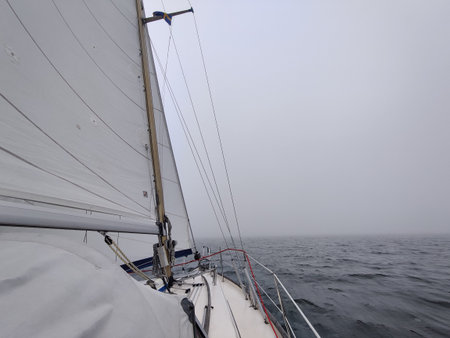 Luxury sailing yacht under genoa and mainsail cutting through waves of the Baltic Sea, Gulf of Finland in fog. Atmospheric maritime scene highlighting motion, adventure, and yachting lifestyleの写真素材