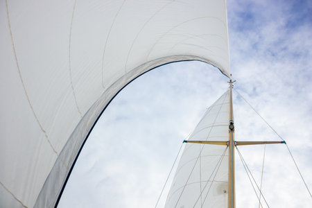 White mainsail and genoa headsail of a sailing yacht catching the wind on calm sea in sunny weather....