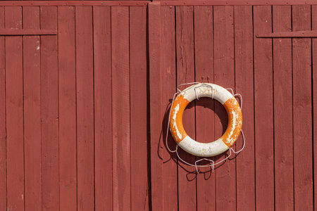 Lifebuoy hanging on wooden wall at seaside location. Classic maritime safety equipment, symbol of rescue, SOS, and nautical protection in coastal environmentの写真素材