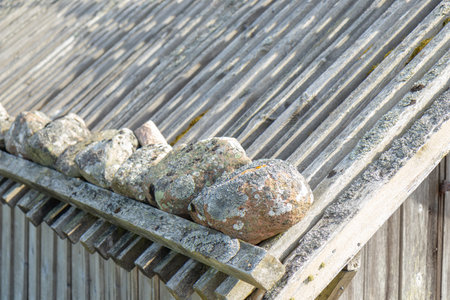 Wooden roof covered with stones. Rustic northern construction showcasing traditional roofing technique, natural materials, and aged patina of timber and rocksの写真素材