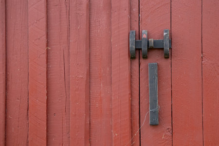 Close-up of metal latch on red-painted wooden door, ecological Nordic tradition of sustainable housing and simple rural architectureの写真素材