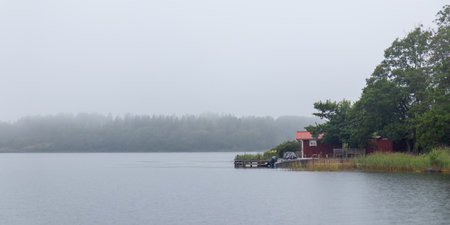 Wooden pontoon with boat and small shed on the Baltic foggy coast, symbolizing Finnish summer cottage life, peaceful holiday retreat, and connection with northern natureの写真素材