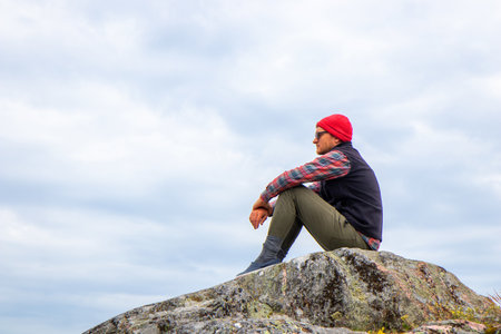 Young man sitting and resting during a hike in Finnish nature. Highlights outdoor adventure, relaxation, and connection with northern wildernessの写真素材