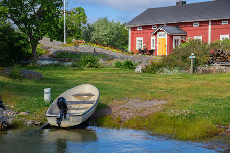 Small boat on the shore beside traditional Finnish cottage in fishing village by the Baltic Sea. Peaceful coastal life, Nordic heritage, and maritime cultureの写真素材