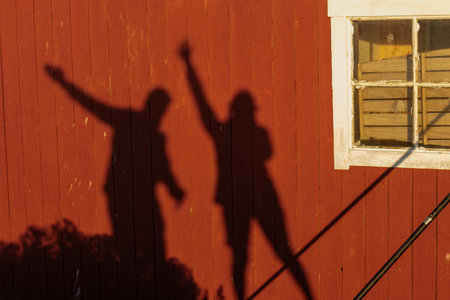 Two playful shadows on a wooden wall. Creative abstract outdoor scene symbolizing joy, friendship, fun moments, and artistic minimalism in natural lightの写真素材