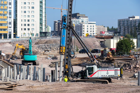 A sunny day at a construction site in a residential area where heavy machinery drives concrete piles...