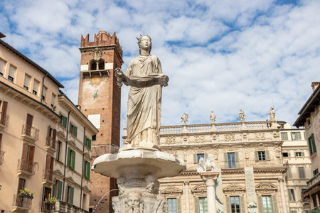 The Fontana di Madonna Verona in Piazza delle Erbe, Italy, a historic fountain featuring the Roman statue, surrounded by medieval buildings and bustling market stallsの写真素材
