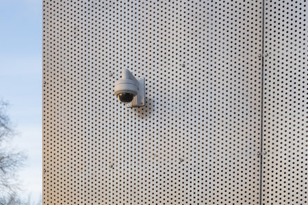 A surveillance security camera installed on the exterior wall of a building, used for monitoring and safety in an urban environmentの写真素材