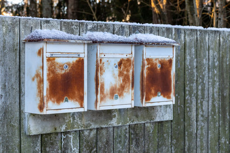Old rusty outdoor mailboxes placed along the street between neighboring residential houses. Metal post boxes used for daily postal delivery in a suburban areaの写真素材