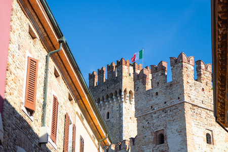 Scaliger Castle (Castello Scaligero) in Sirmione, Italy, a historic lake fortress from the Scaliger era, gateway to the medieval town center on Lake Garda, with Italian flagの写真素材