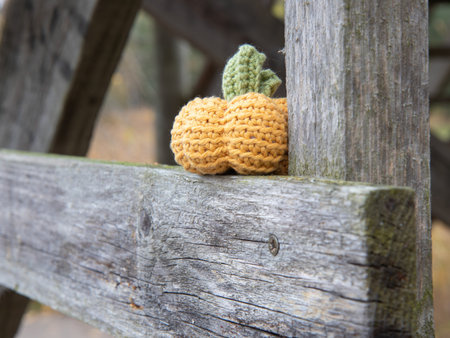 Handmade crochet pumpkin toy in yellow and green yarn on a rustic wooden surface. Perfect for fall or Halloween decor, crafted using amigurumi techniquesの写真素材