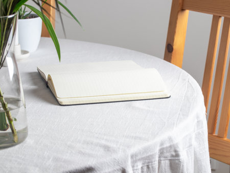 Open black hardcover notebook on a white tablecloth. Blank off-white pages with sewn binding lie...