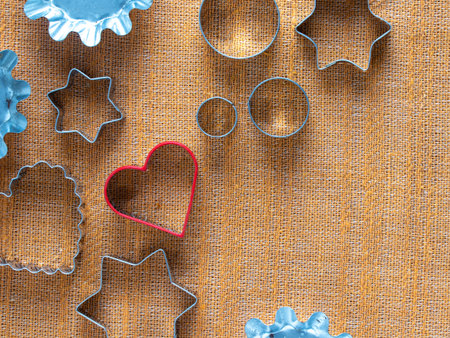 Various metal cookie cutters on a textured surface, including circles, stars, scalloped, and red heart shapes. Used for baking cookies, fondant, or play-doughの写真素材
