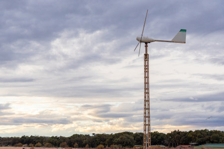 A wind turbine, aerogenerator stands tall in an open field beneath a dramatic, cloudy sky,...