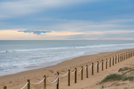 Protected dunes at El Moncayo Beach in Guardamar del Segura, Spain, fine sand. Wooden walkways and rope fencing guide visitors, prevent erosion, and protect fragile coastal ecosystemsの写真素材