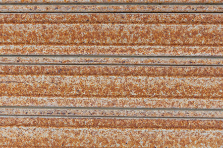 Close-up of a rusted corrugated metal surface with heavy oxidation, showing brown and orange...