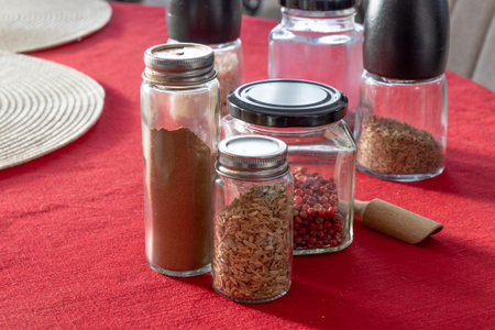 A collection of glass spice jars filled with various seasonings and spices, neatly arranged on a red...
